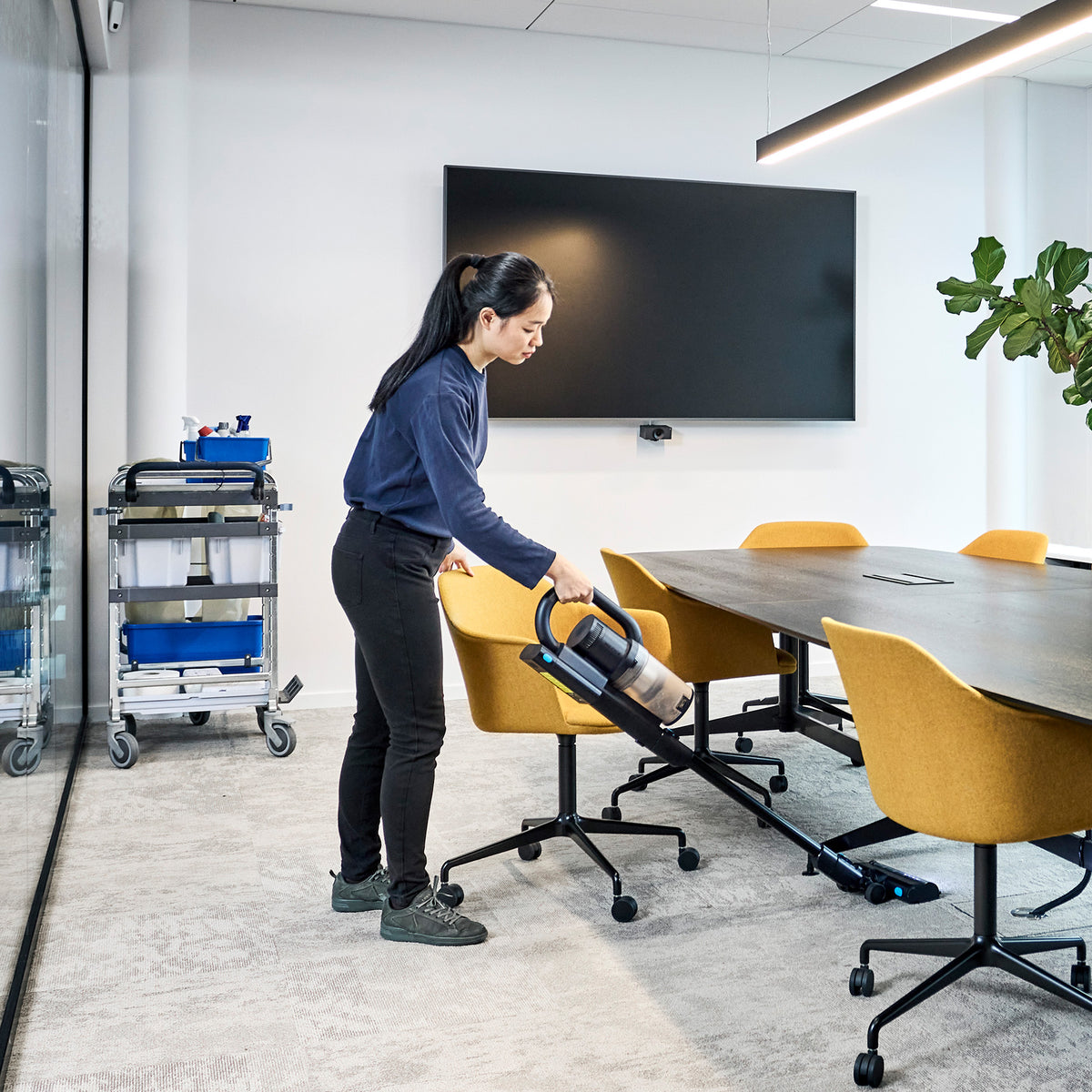 Aspirador vertical Nilfisk VU200 HEPA com design ergonômico e bateria, exibido em ambiente doméstico.